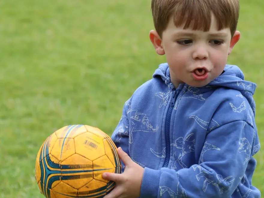 A toddler holding a football on the grass at a uSports nursery session