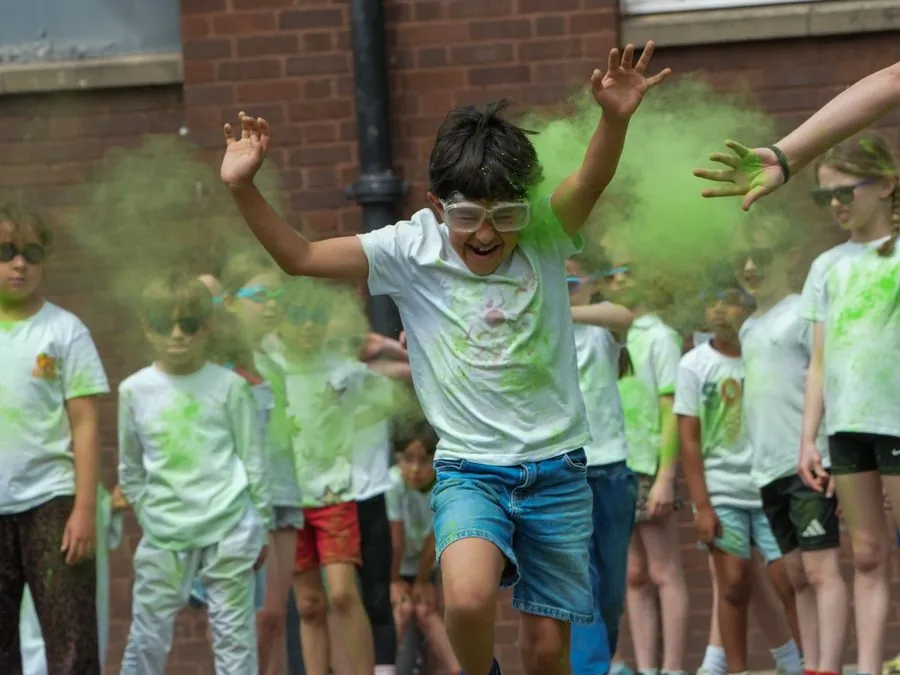 A laughing boy in safety goggles running through a cloud of green powder paint, with other children watching