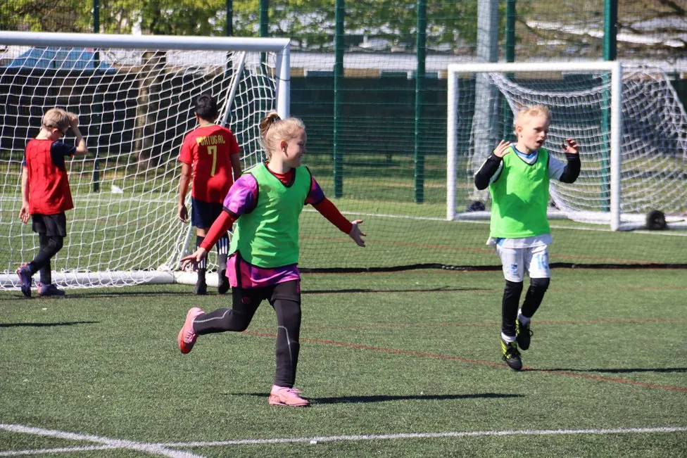 Children in bibs celebrating during a football game on a 3G pitch